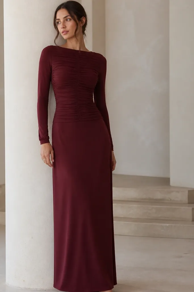 A burgundy long sleeve maxi dress with ruched detailing across the bust and upper torso. The skirt hangs straight and the sleeves are fitted with a narrow cuff.