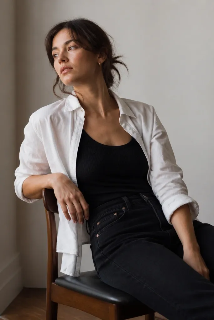A black tank with straight-leg dark jeans, layered with a white button-up worn open. The button-up is slightly wrinkled in a deliberate, casual way.